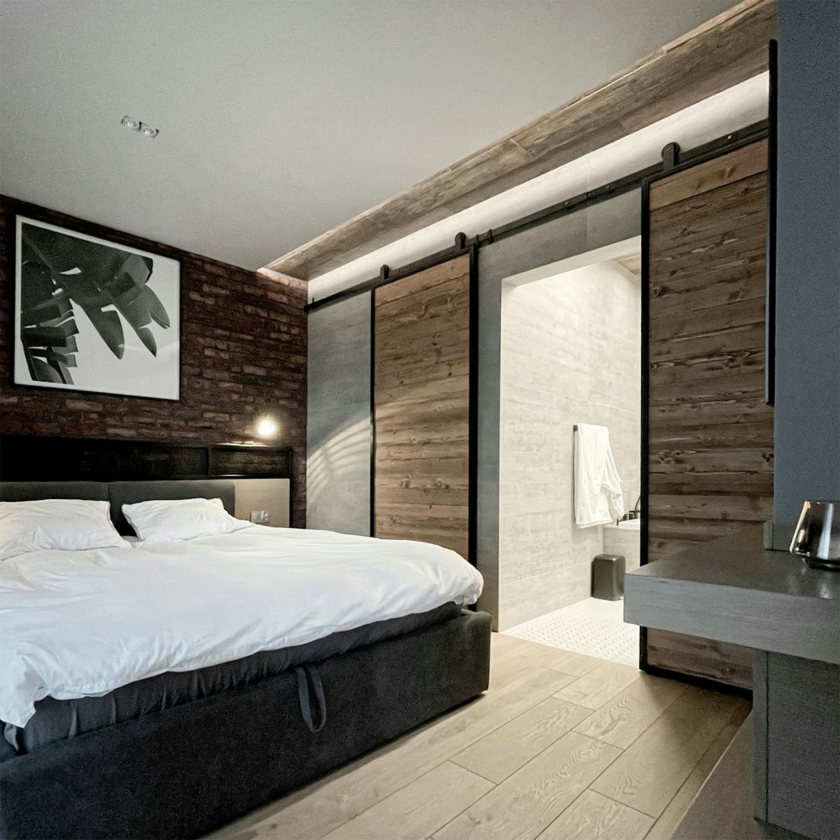Schiebetür zum Badezimmer in einem industriellen Schlafzimmer, roter Backstein an der Wand im Schlafzimmer