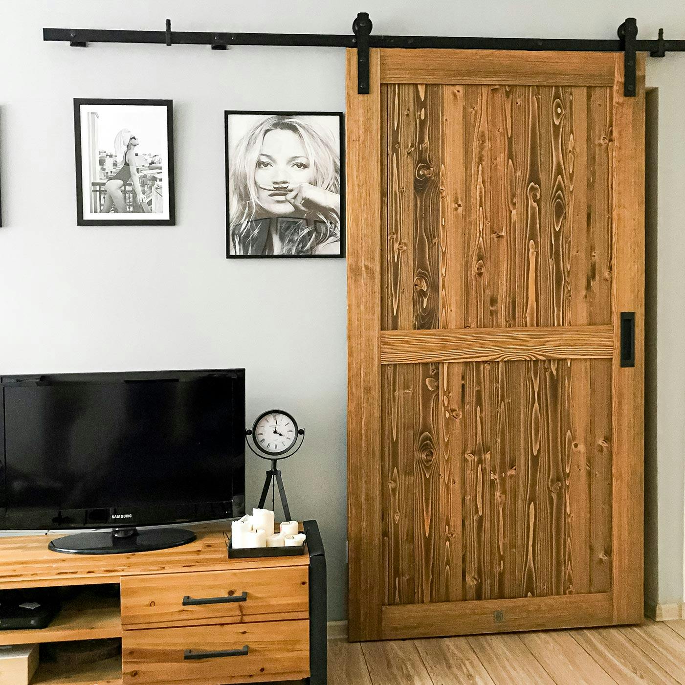 sliding doors in a small apartment, wooden door installed on black sliding system, black and white posters on the wall, steel and wood TV cabinet, black decorative standing clock