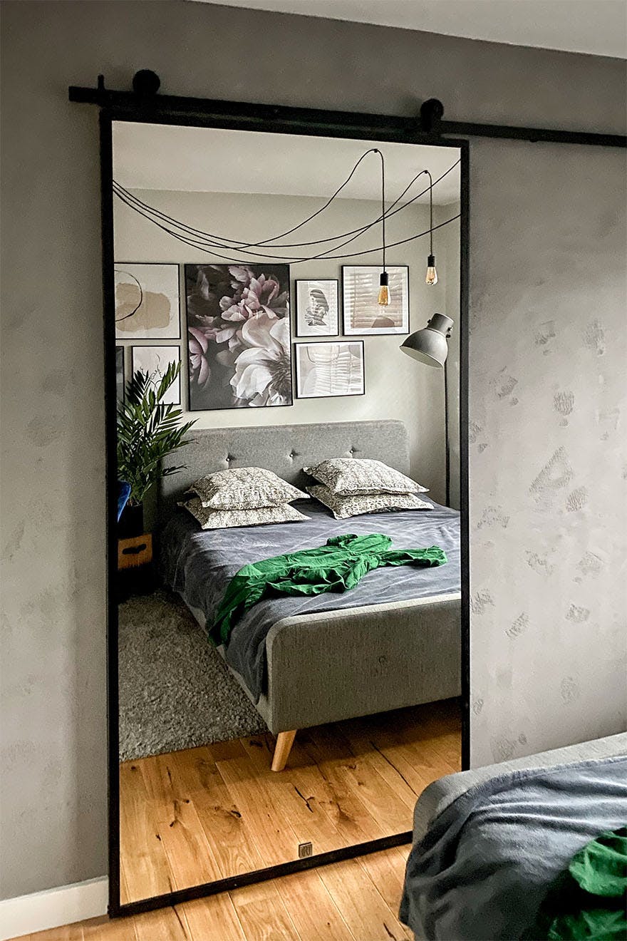 sliding door with a mirror in a metal frame on a grey wall in a loft-style bedroom in grey colours