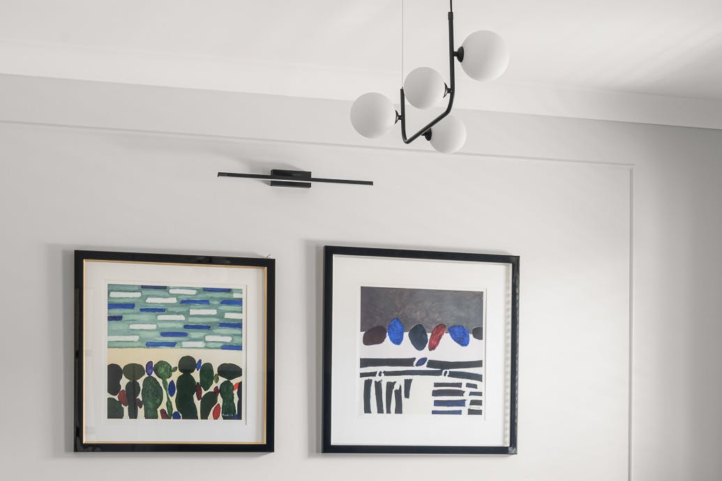 Lustre en métal et peintures dans des cadres noirs contre un mur clair