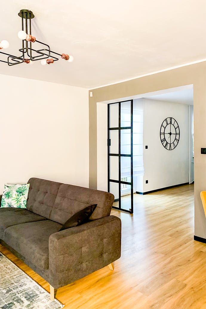 intérieur loft, porte vitrée dans un cadre métallique, porte coulissante en verre, lampe industrielle dans le salon, canapé gris, salon ouvert, horloge murale industrielle