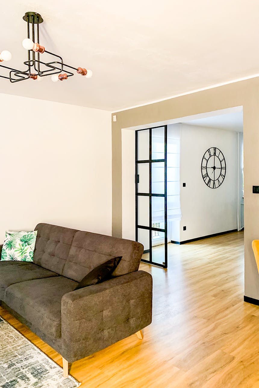 Loft-Innenraum, Glastür in einem Metallrahmen, Glasschiebetür, Industrielampe im Wohnzimmer, graues Sofa, offenes Wohnzimmer, industrielle Wanduhr