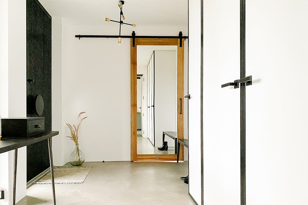 Une lampe industrielle, une table minimaliste noire et une porte coulissante avec un miroir dans le vestibule