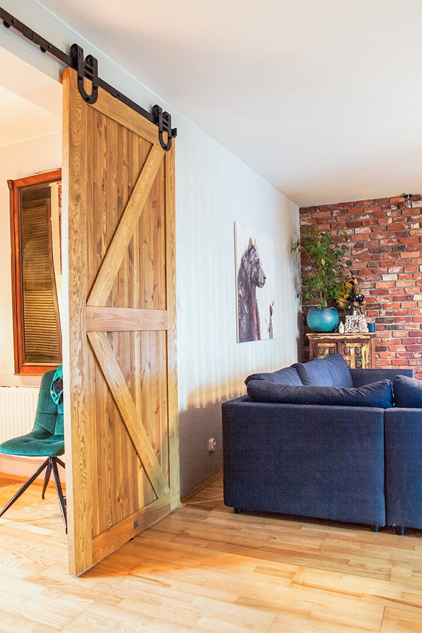 rustikale Holztür, Schiebetür aus gebürstetem Holz, barn door, Schiebetür mit einem Hufeisen, blaues Sofa im Wohnzimmer, Ziegel an der Wand
