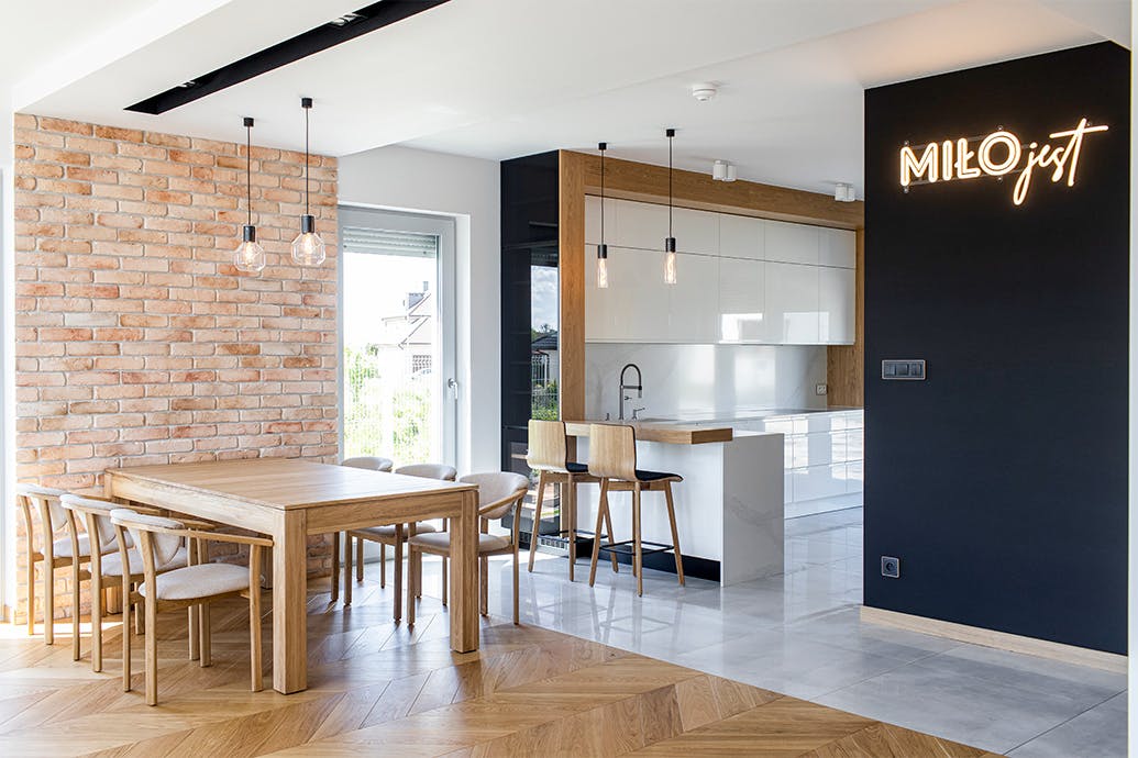une grande table en bois contre un mur de briques dans une salle à manger ouverte combinée à une cuisine moderne