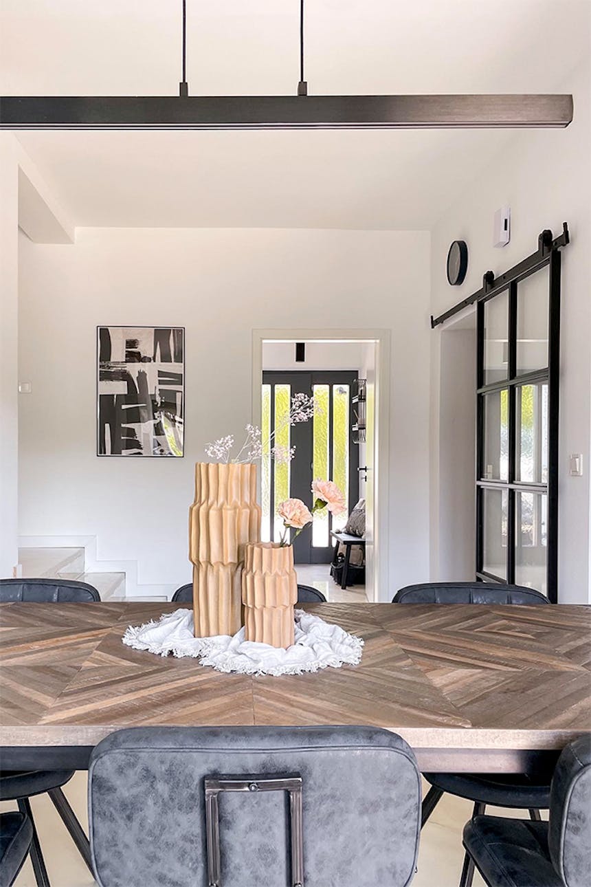 dekoracyjne wazony na dużym stole w jadalni oświetlonym długą minimalistyczną lampą