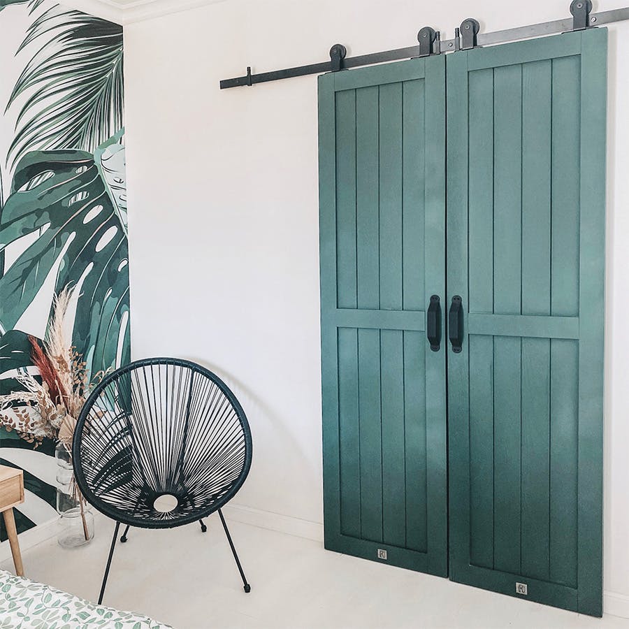 green doors, walk-in closet door, sliding door, black sliding door system, black openwork armchair, solid wood door, white and green in the bedroom, botanical wallpaper, plant wallpaper