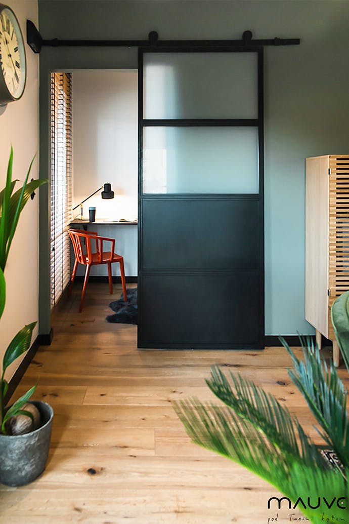 Des portes coulissantes industrielles remplies de verre opale s'ouvrent sur un petit coin de travail avec un bureau