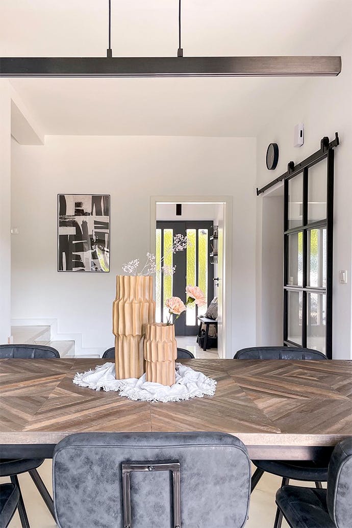 Vases décoratifs sur une grande table à manger éclairée par une longue lampe minimaliste