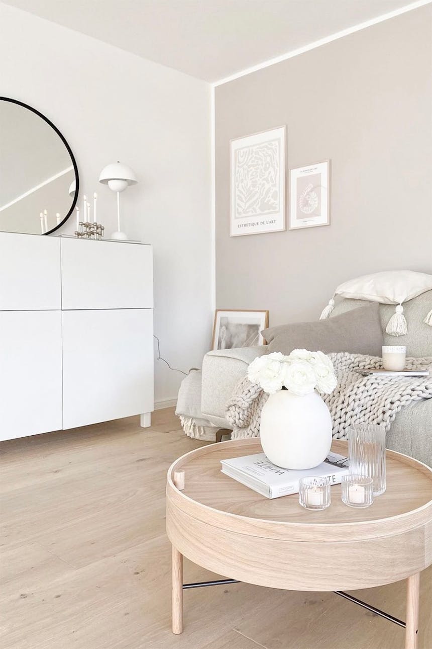 runder heller Holztisch im nordischen Stil, weiße Blumen in einer weißen Vase auf dem Beistelltisch, weiße Kommode im nordischen Stil, beiges Sofa
