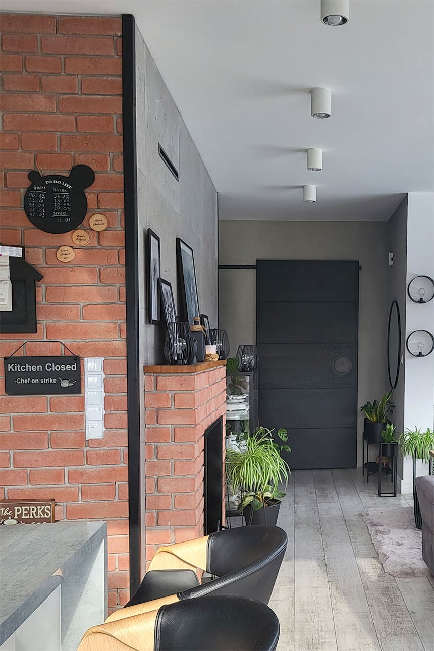 czerwona cegła na ścianie i wokół kominka oraz czarne drzwi przesuwne w salonie