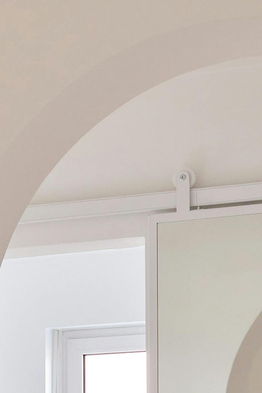 Ein Detail des weißen Schiebesystems für Spiegeltüren, das direkt unter dem architektonischen Rundbogen zu sehen ist.