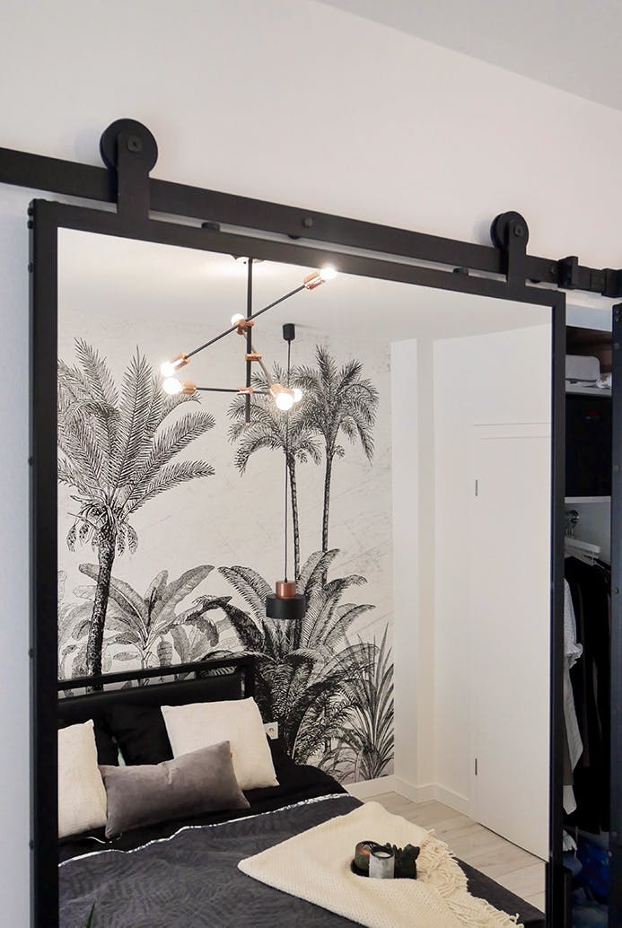 Porte coulissante avec un miroir dans un cadre en métal montrant un fragment de chambre dans un style moderne