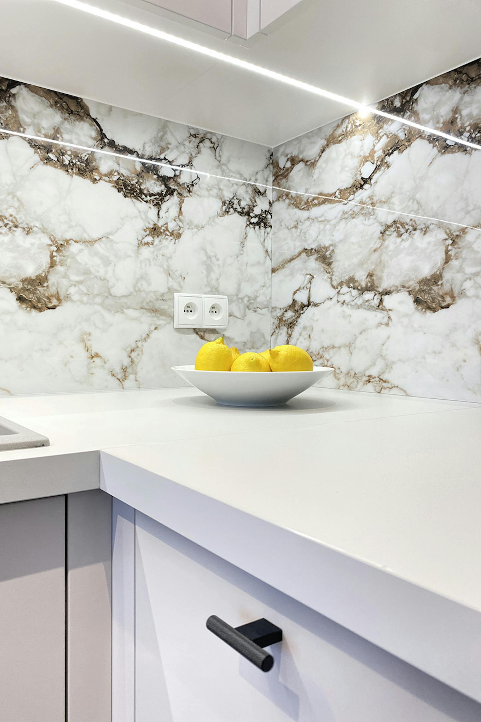 Fliesen mit Steinmotiv über der Küchenarbeitsplatte, weiße Küchenmöbel, modernes Apartment