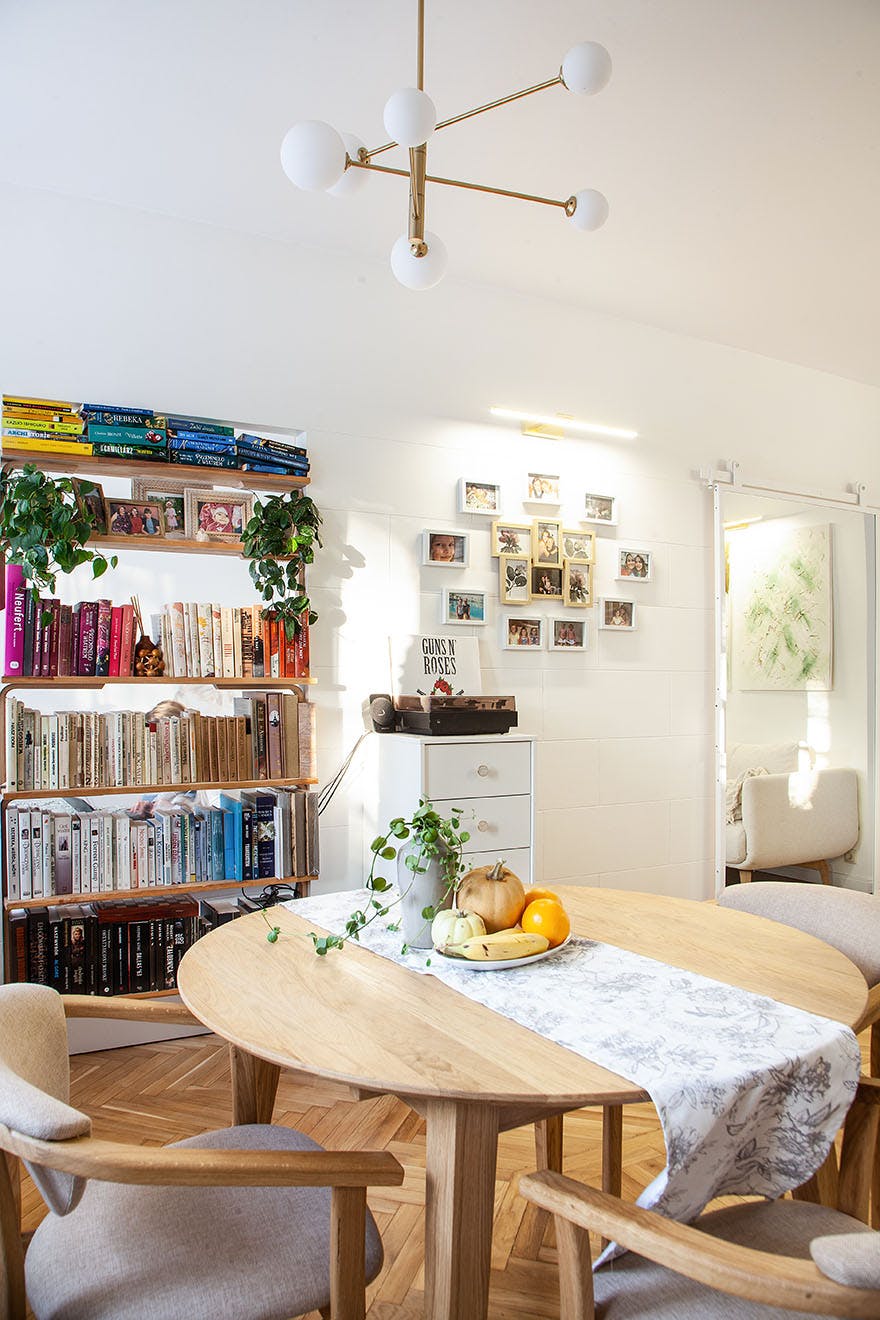 a round wooden table and a bookshelf with books in the interior of a small apartment