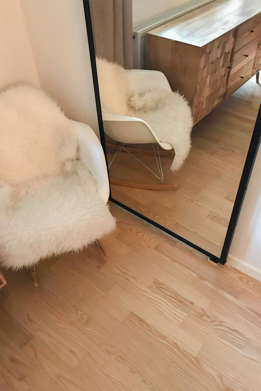 un grand miroir dans un cadre métallique à côté d'un fauteuil blanc