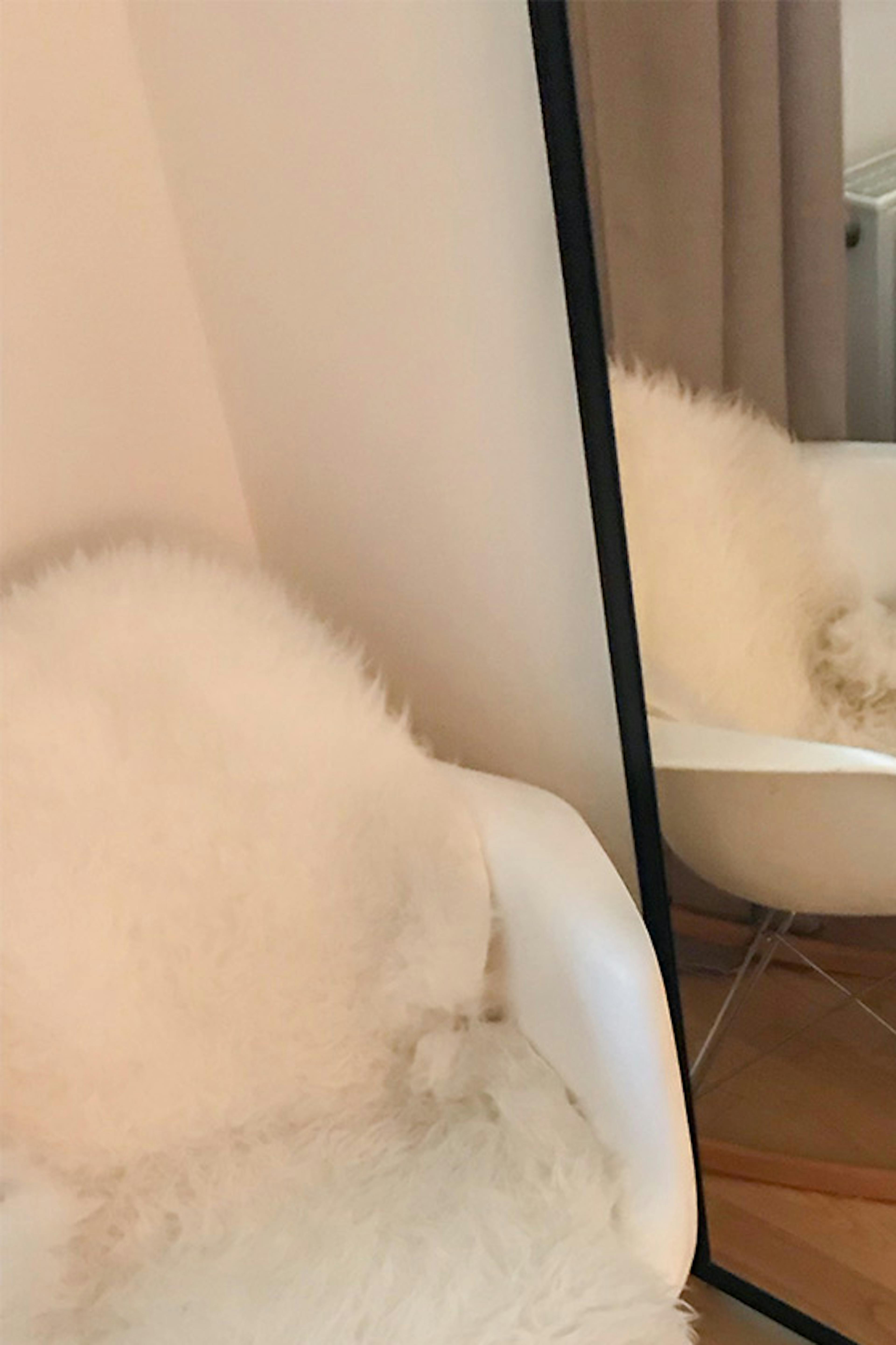un grand miroir dans un cadre métallique à côté d'un fauteuil blanc