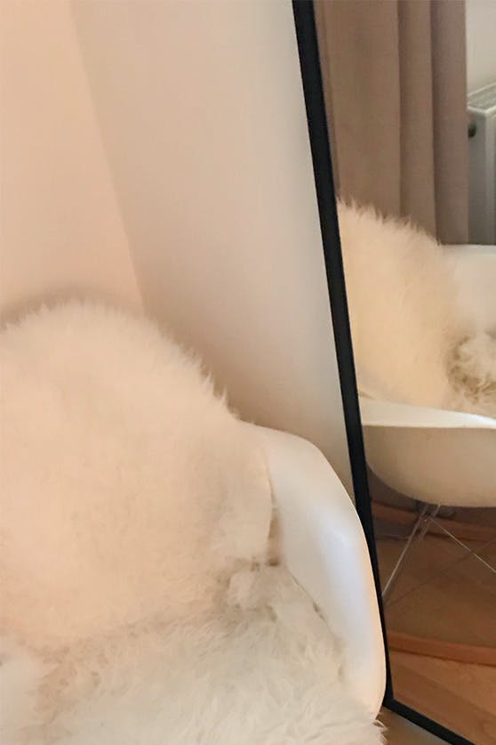un grand miroir dans un cadre métallique à côté d'un fauteuil blanc