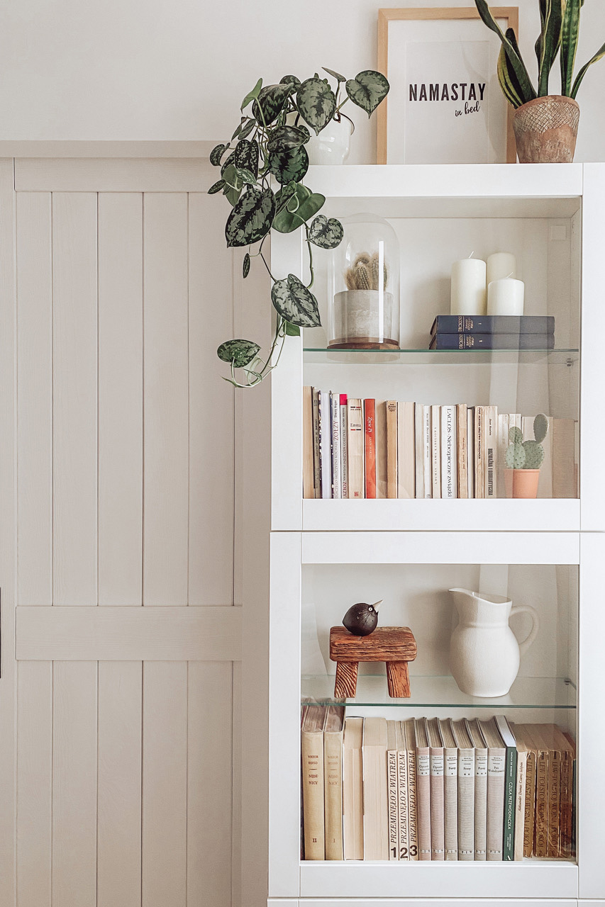 eine weiße Vitrine voller Bücher und Dekorationen vor einer weißen Wand im Schlafzimmer