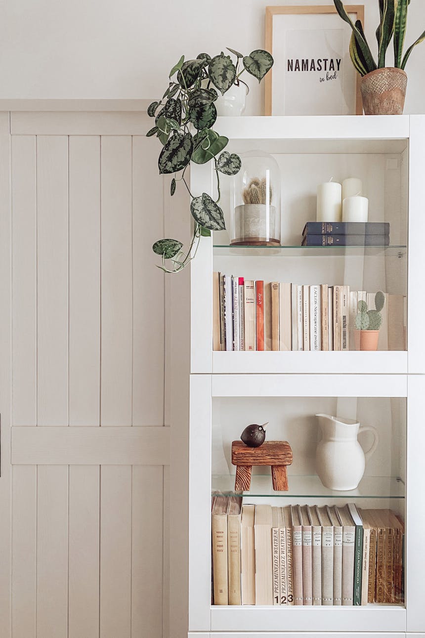 eine weiße Vitrine voller Bücher und Dekorationen vor einer weißen Wand im Schlafzimmer