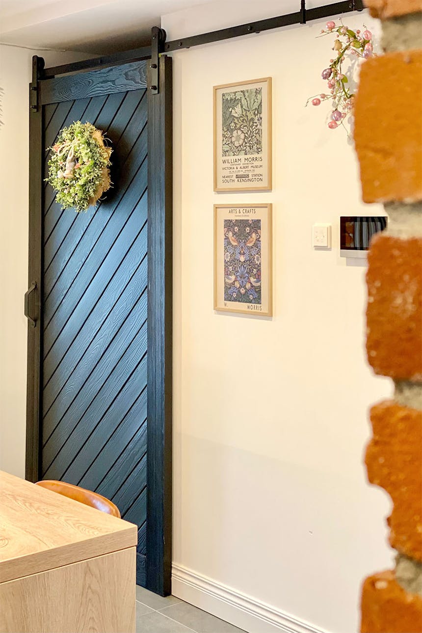 Schiebetür für die Speisekammer, schwarze Schiebetür aus Massivholz, dekorativer Kranz an der Tür, roter Backstein an der Wand, dekorative Gemälde an der weißen Wand