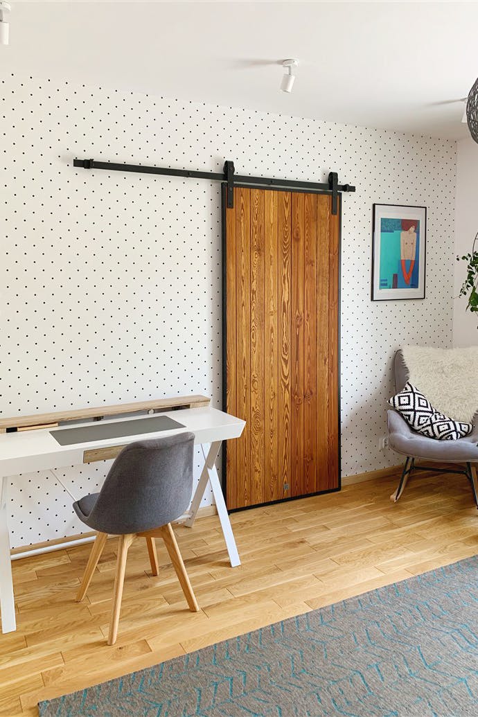 une chaise grise à côté d'une coiffeuse blanche et une porte coulissante en bois sur fond de mur à pois