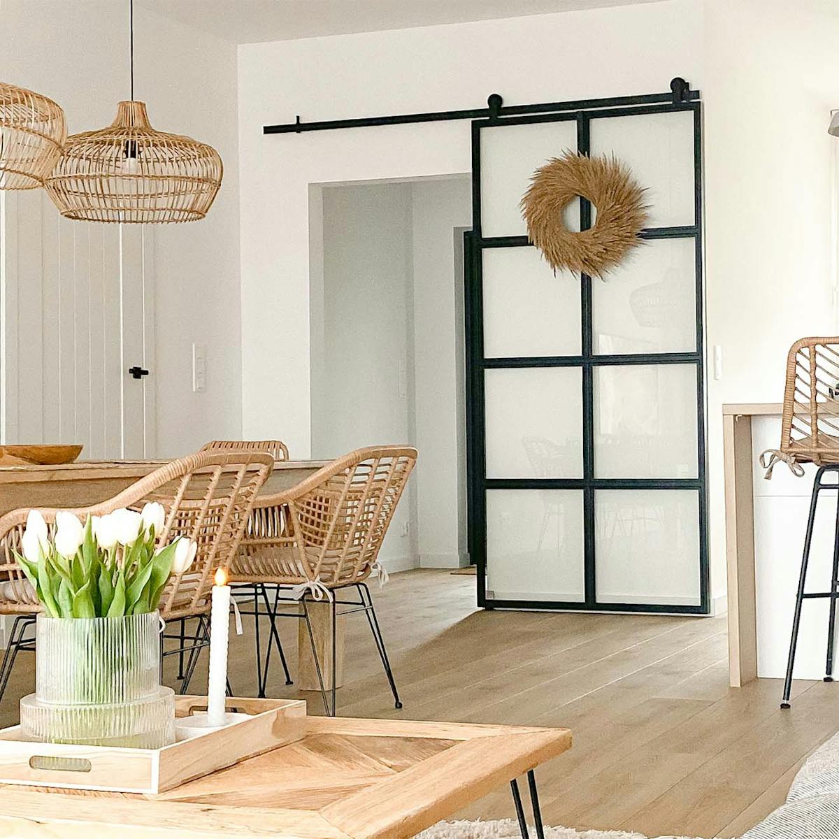 rattanowe krzesła na metalowych nogach, duży drewniany stół, lampy wiszące z wiklinowym abażurem oraz szklane drzwi przesuwne z metalową ramą