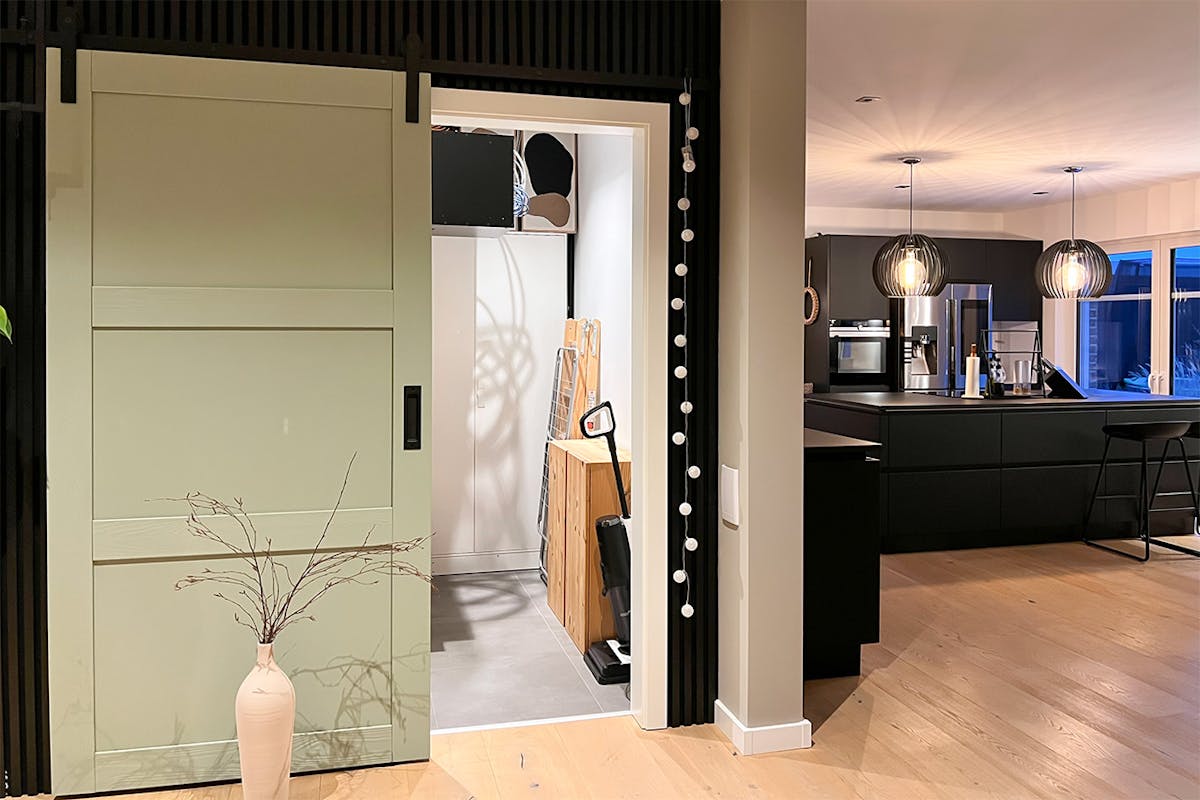 Salbeigrüne Schiebetüren zur Speisekammer neben der modernen Küche mit schwarzen Möbeln