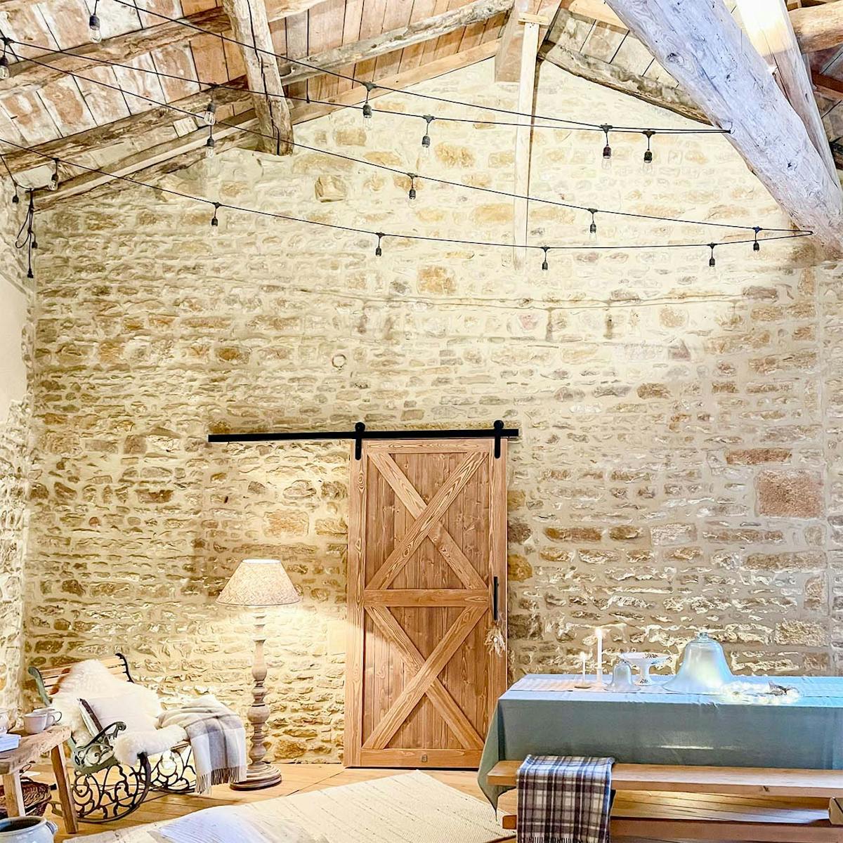 drewniany stół, ławy, fotel bujany i drzwi przesuwne na zadaszonym tarasie obudowanym ścianami z naturalnego kamienia