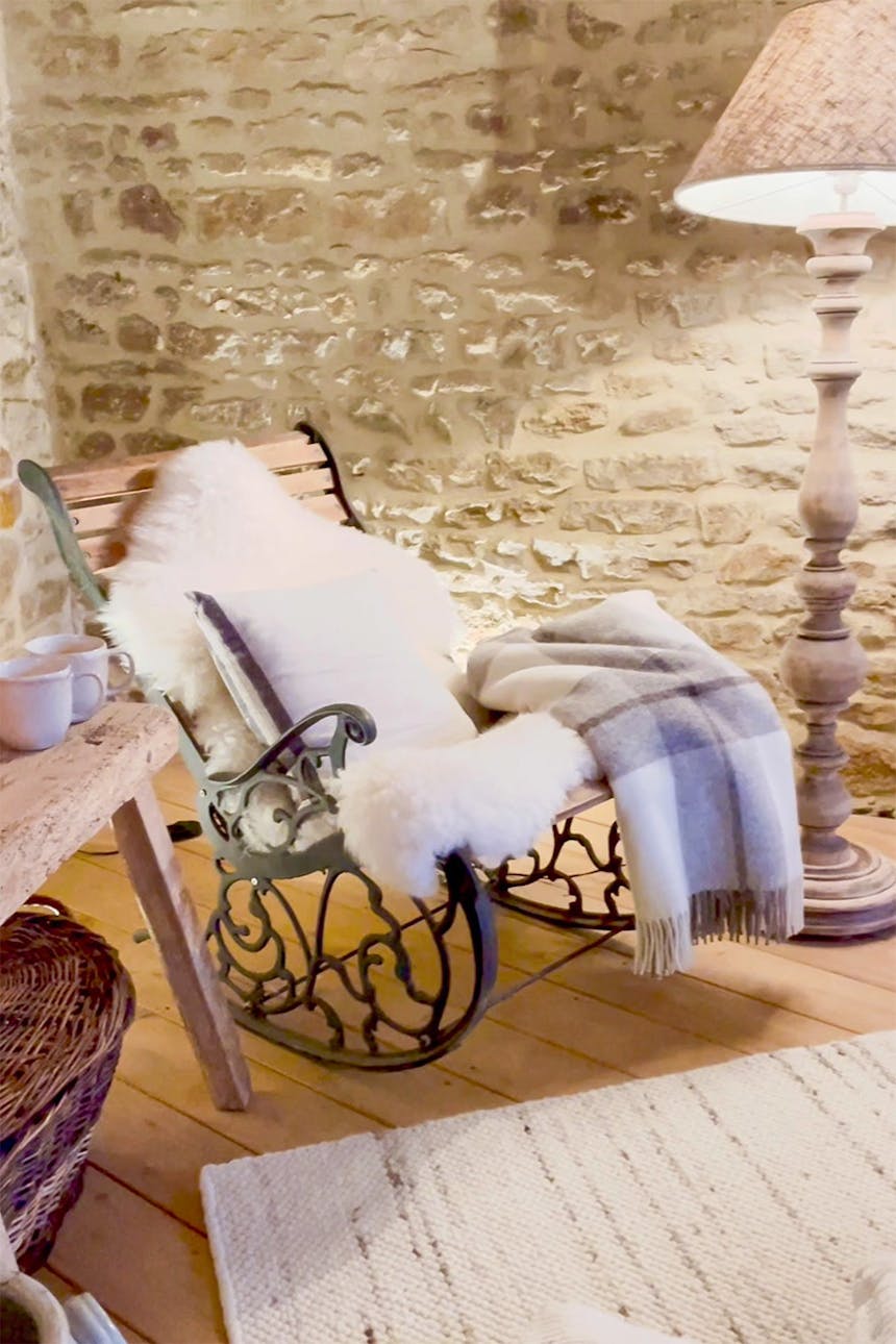 fotel bujany przykryty miękkimi kocami obok lampy stojącej z dużym abażurem