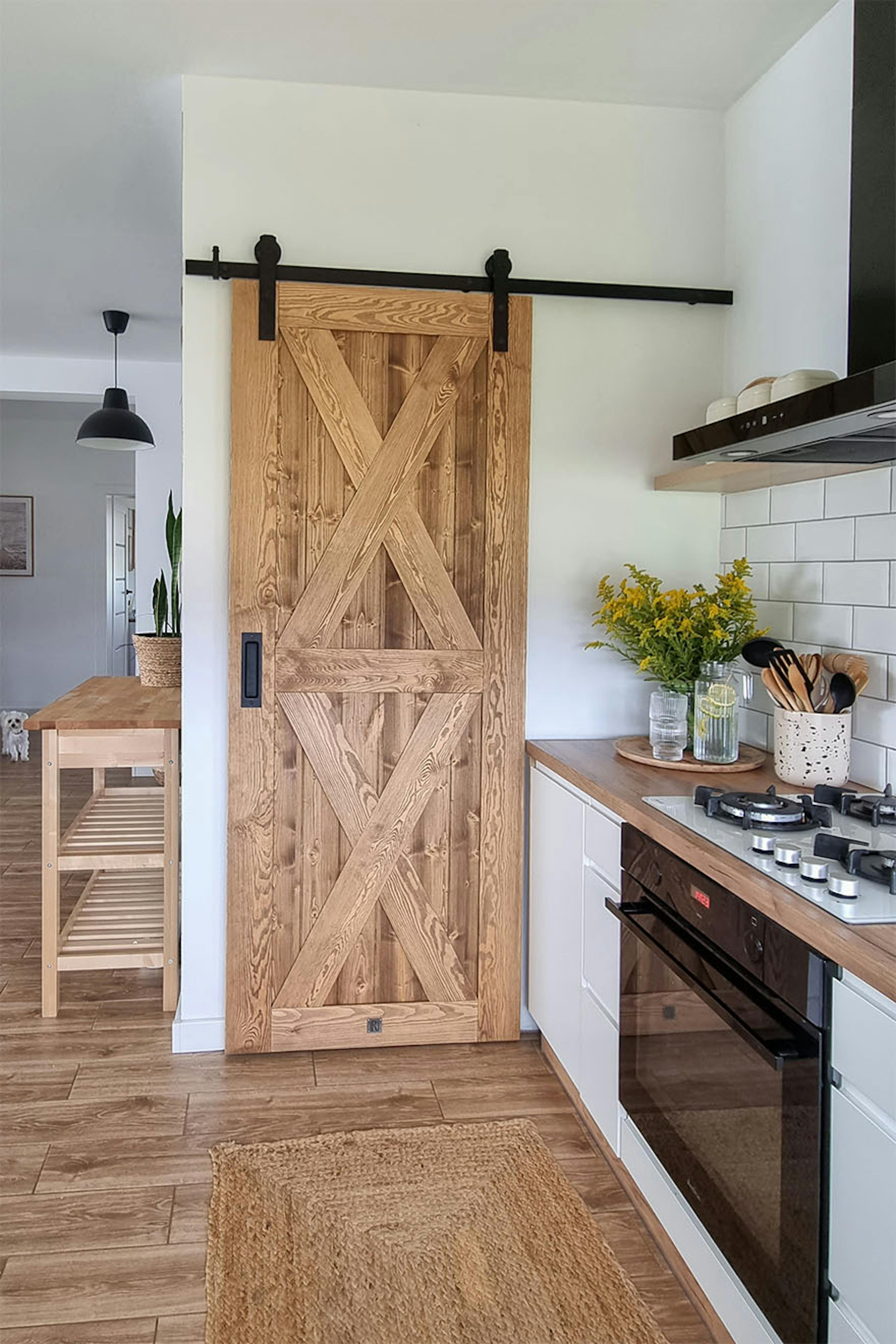 portes coulissantes en bois fermant le garde-manger à côté d'une cuisine lumineuse avec des armoires blanches de style scandinave