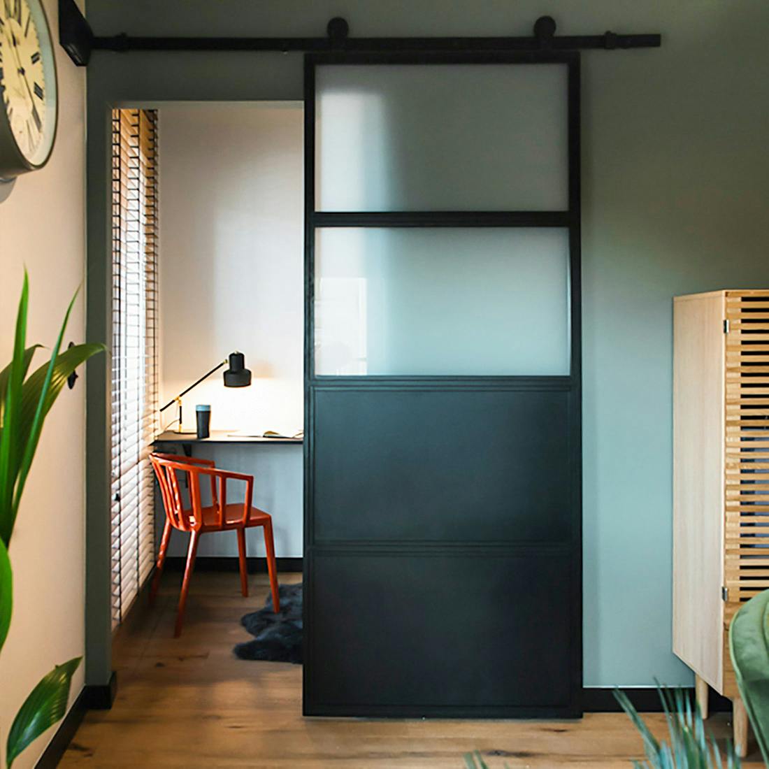 Des portes coulissantes industrielles remplies de verre opale s'ouvrent sur un petit coin de travail avec un bureau