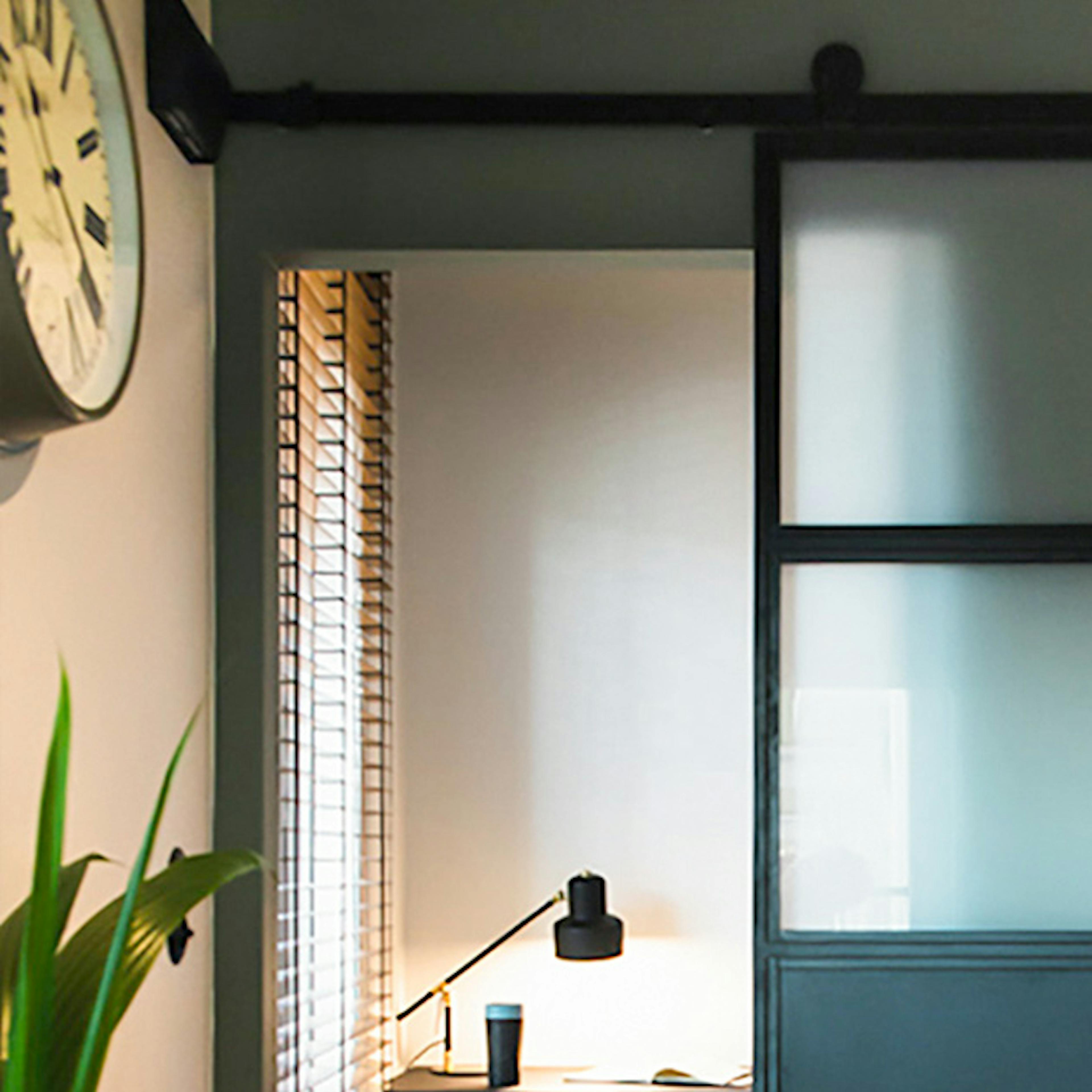 Des portes coulissantes industrielles remplies de verre opale s'ouvrent sur un petit coin de travail avec un bureau