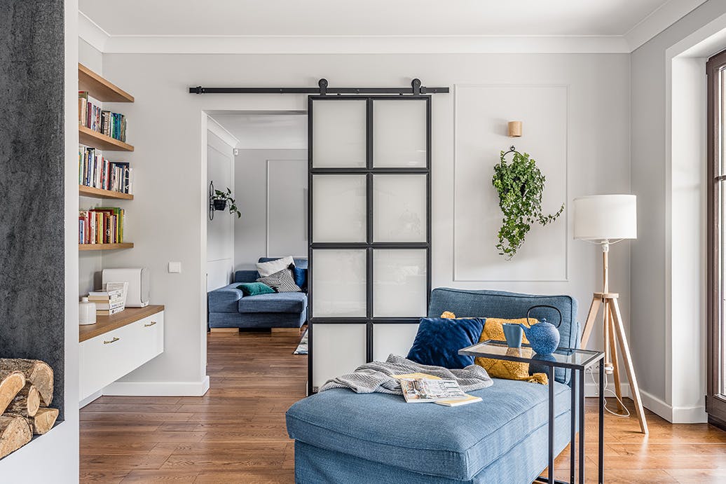 Coin lecture avec un canapé bleu, séparé du salon par une porte coulissante en verre opale
