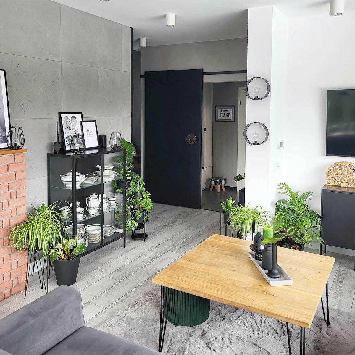 ein holztisch auf metallbeinen, eine schwarze glasvitrine und schwarze schiebetüren in einem modernen wohnzimmer