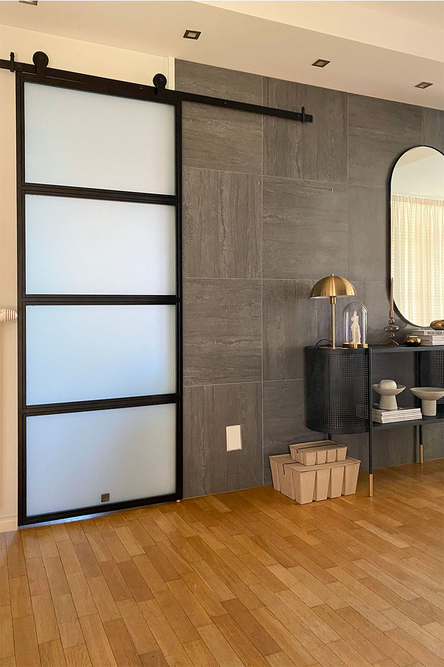 industrielle Schiebetür für die Küche, Glastür zwischen Küche und Flur, Graphitfliesen an der Wand im Flur, goldene Lampe an der schwarzen Konsole im Flur