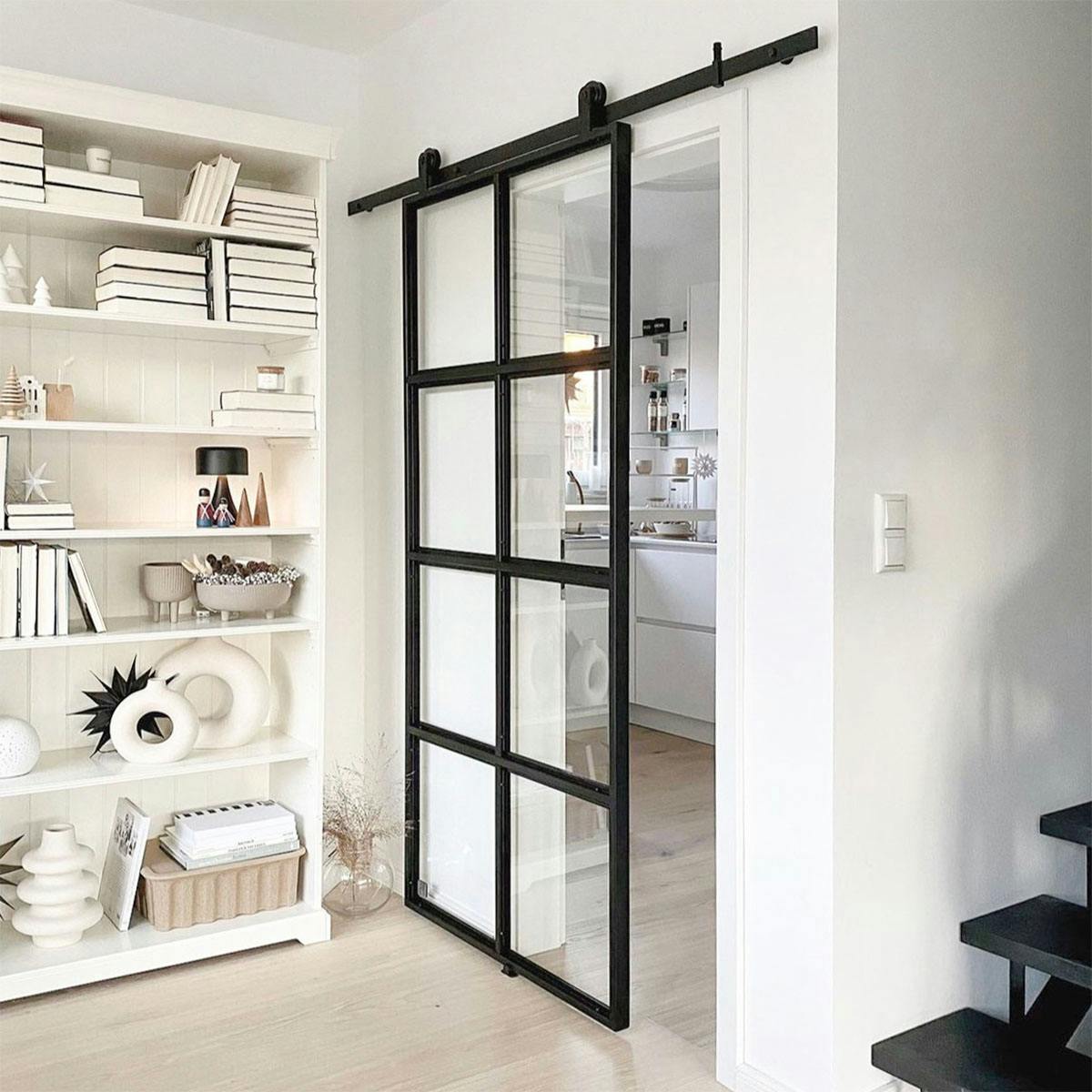 Dekorationen im nordischen Stil auf einem weißen Bücherregal, Glasschiebetür für weiße Küche, Glastür in schwarzem Metallrahmen