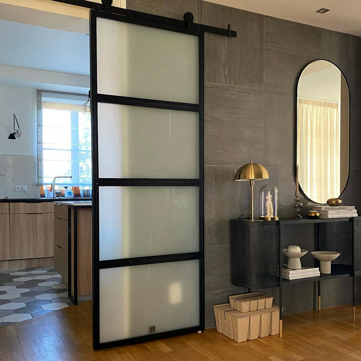 Loft Türen mit glas, Metalltür mit glas für die Küche, helle Küche mit Insel, grafitfliesen an der wand, goldene Lampe auf einer schwarzen Konsole, schwarze durchbrochene Konsole mit spiegel in der flur