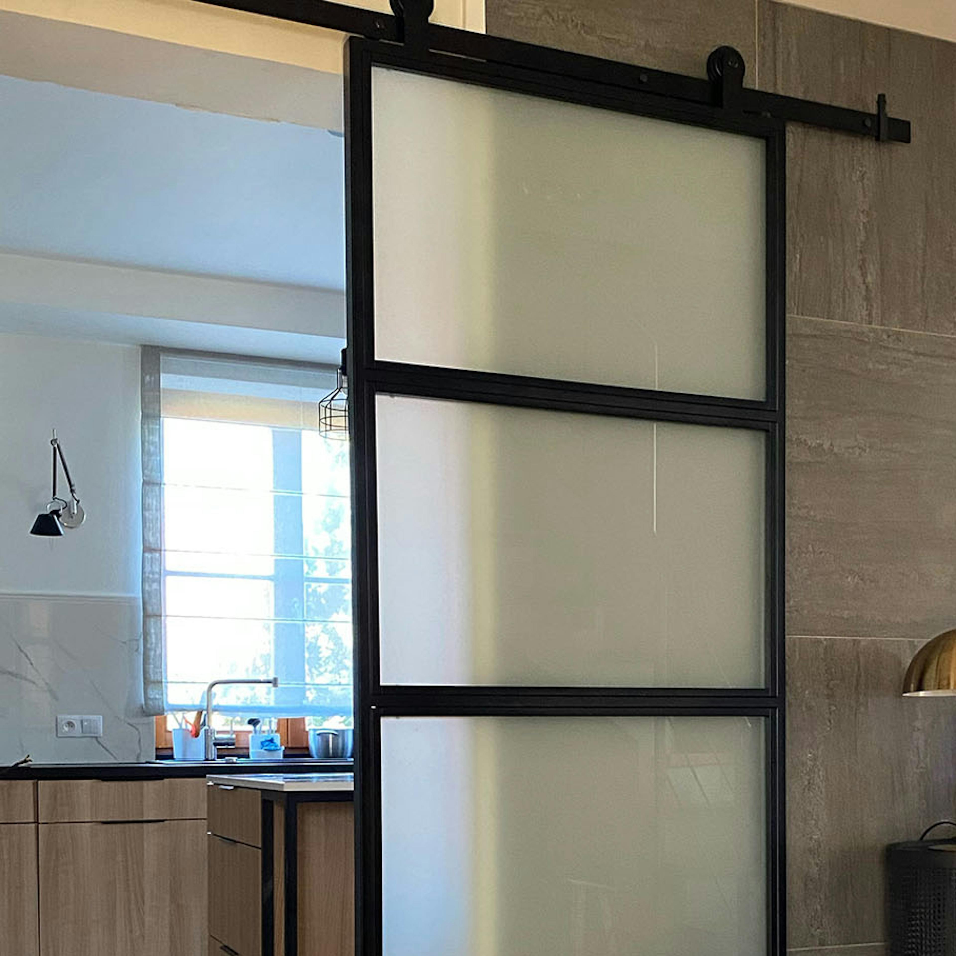 porte coulissante en métal vitré séparant la cuisine du hall et une console noire contre un mur en carreaux de graphite