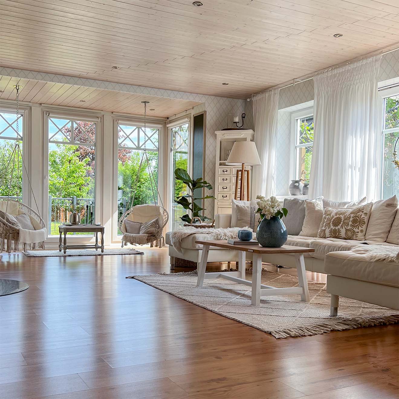 przestronny salon z drewnianą podłogą, jasną sofą i dużymi oknami