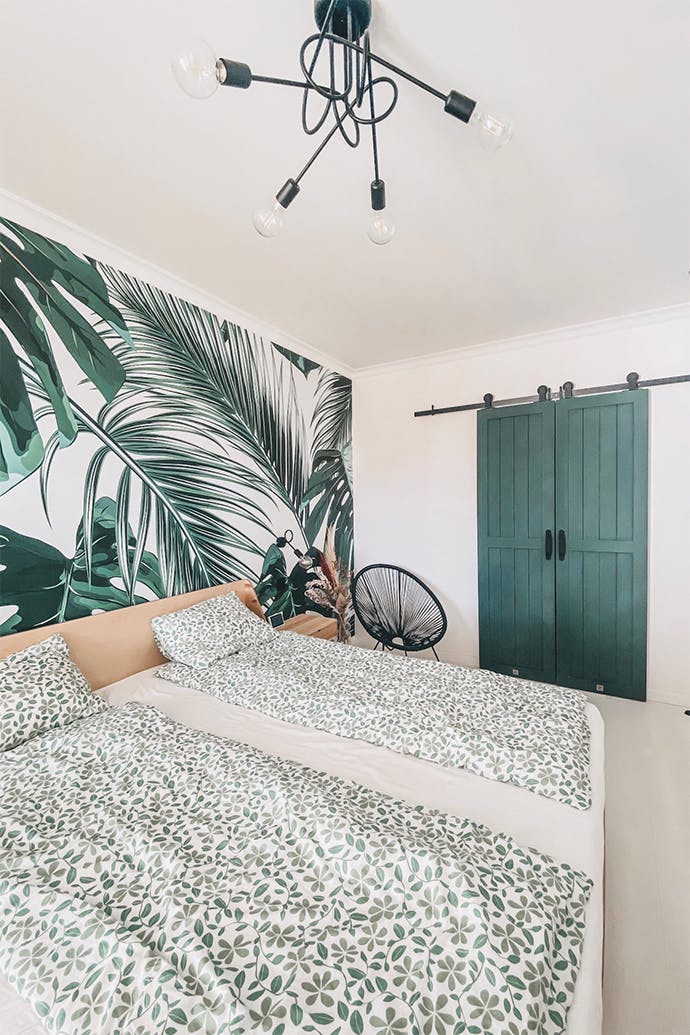 chambre lumineuse avec papier peint végétal décoratif et une armoire cachée derrière des portes coulissantes vertes