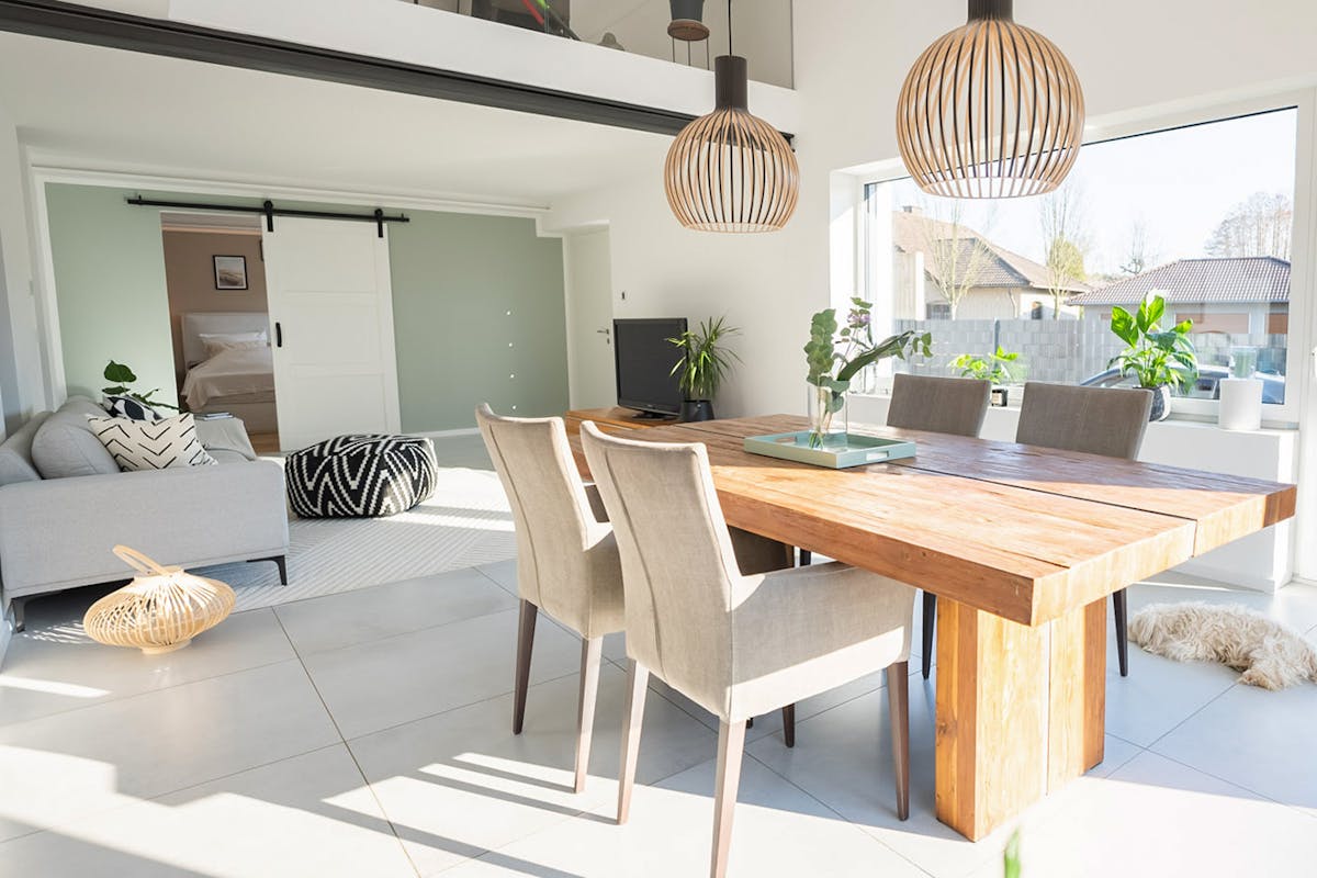 Modernes und geräumiges Wohnzimmer, massiver Esstisch, beige Polsterstühle, graues Sofa, weiße Schiebetüren