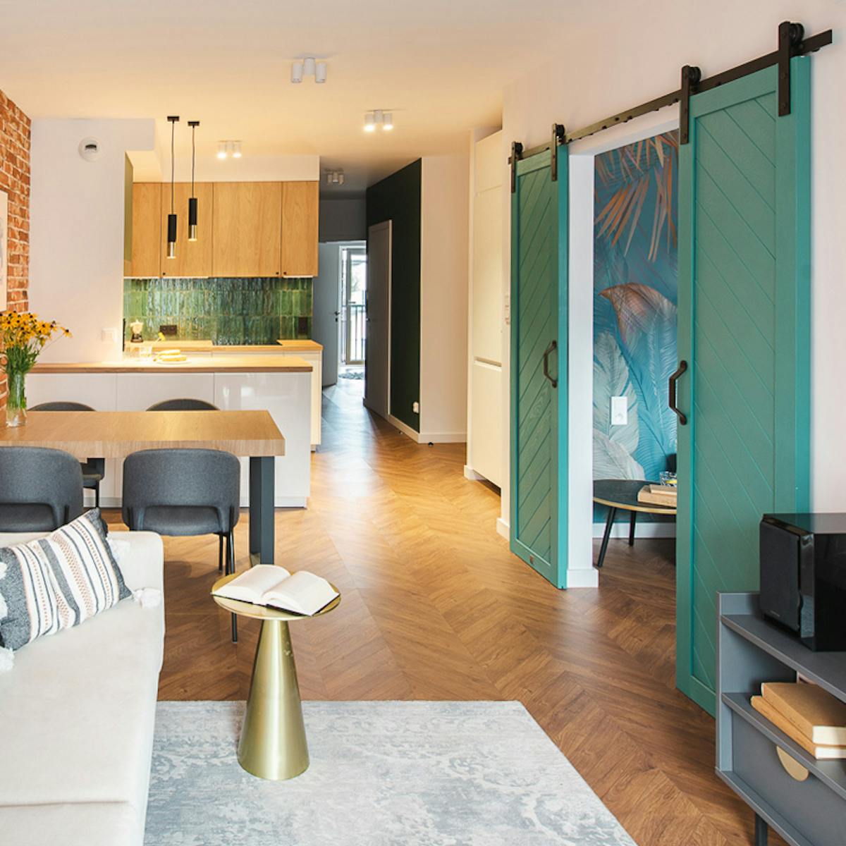 ein Wohnzimmer mit Küchenzeile, das durch eine türkisfarbene Schiebetür vom Schlafzimmer getrennt ist