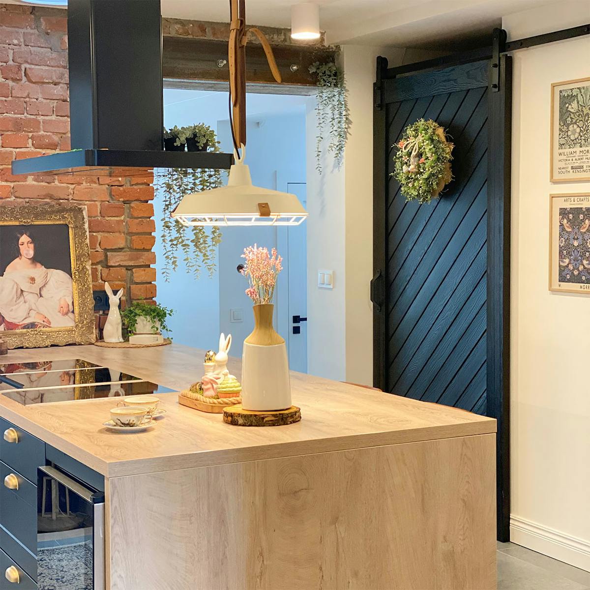 große Kücheninsel mit Holzplatte, schwarze Haube über der Kücheninsel, Schiebetür zur Speisekammer, dekorativer Kranz an der Tür