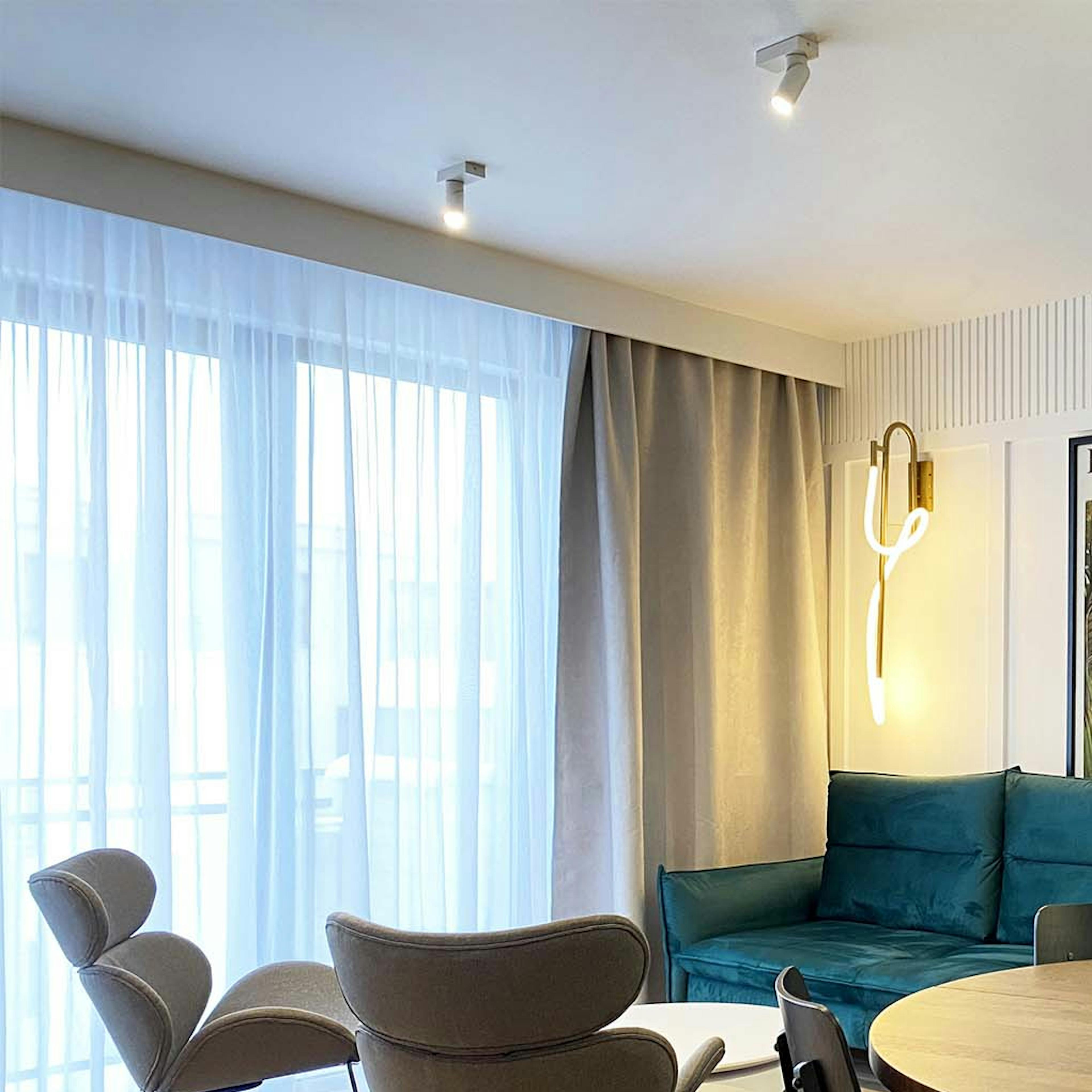 canapé émeraude, fauteuils gris sur cadre noir et table ronde dans le salon-salle à manger d'un appartement moderne