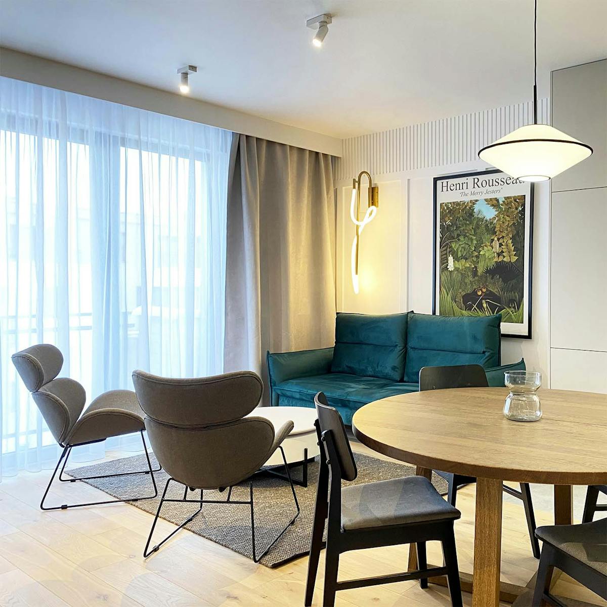 szmaragdowa sofa, szare fotele na czarnym stelażu oraz okragły stół w części jadalniano-salonowej nowoczesnego mieszkania