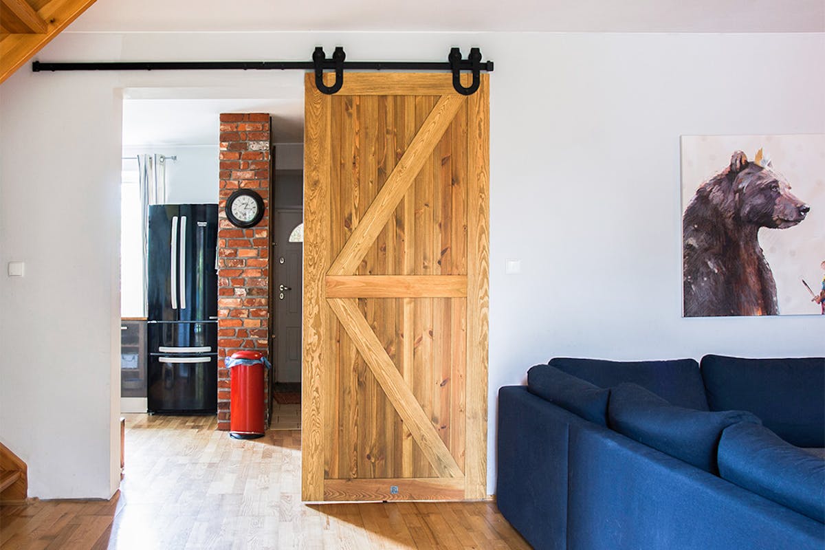 rustikale Holztür, Schiebetür aus gebürstetem Holz, barn door, Schiebetür mit einem Hufeisen, großes blaues Sofa im Wohnzimmer, Schiebetür zur Küche