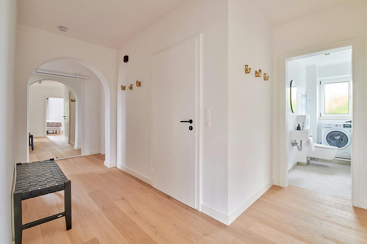 Ein breiter Flur in der Wohnung, der einen gewölbten Durchgang mit verspiegelten Schiebetüren sowie den Eingang zur Toilette zeigt.