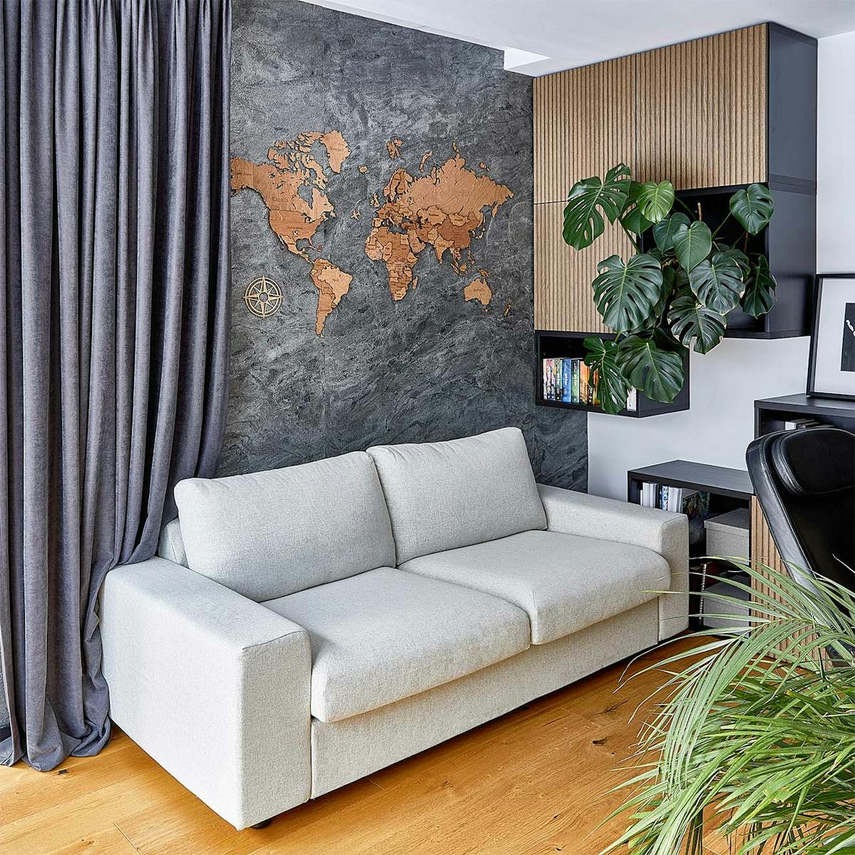 hellgraues Sofa vor einer mit Steinfurnier und einer hölzernen Weltkarte dekorierten Wand