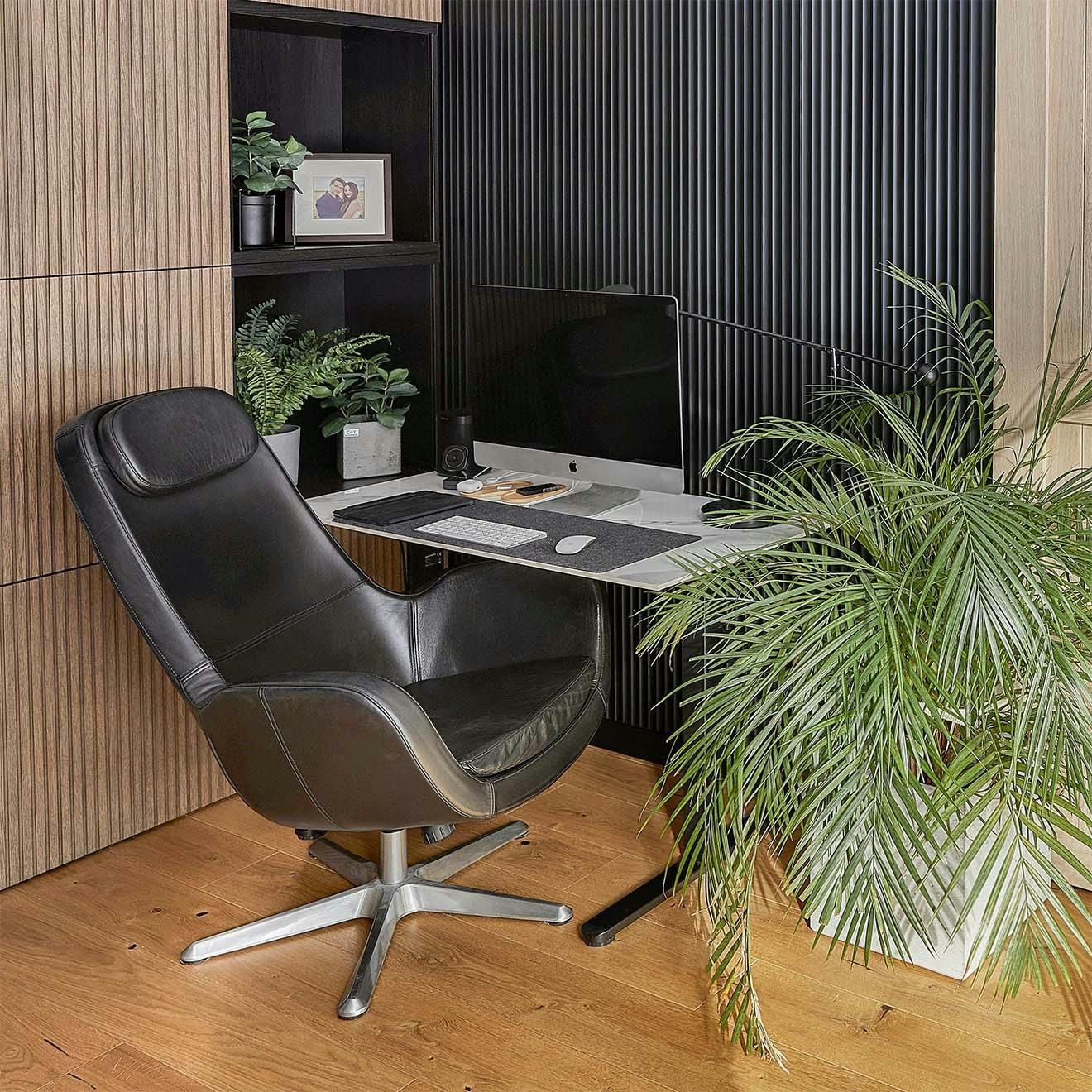black leather armchair, small desk, large potted plant and black wall slats in home office